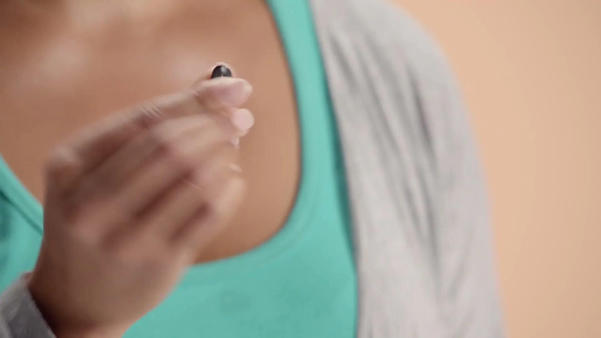 A woman in a teal top and grey cardigan holds a small black hair tie between her fingers.