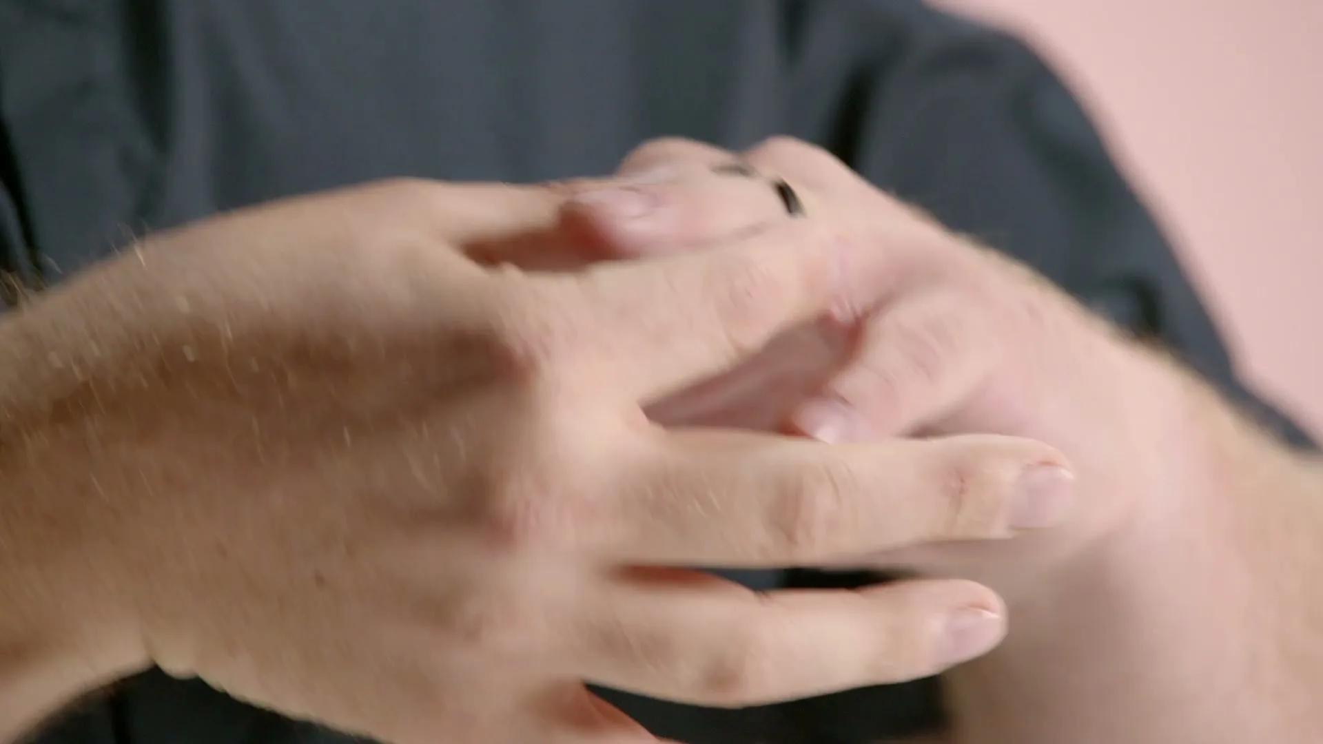 A man with fair skin and a dark shirt holds a small black ring between his fingers, then puts it on his ring finger.