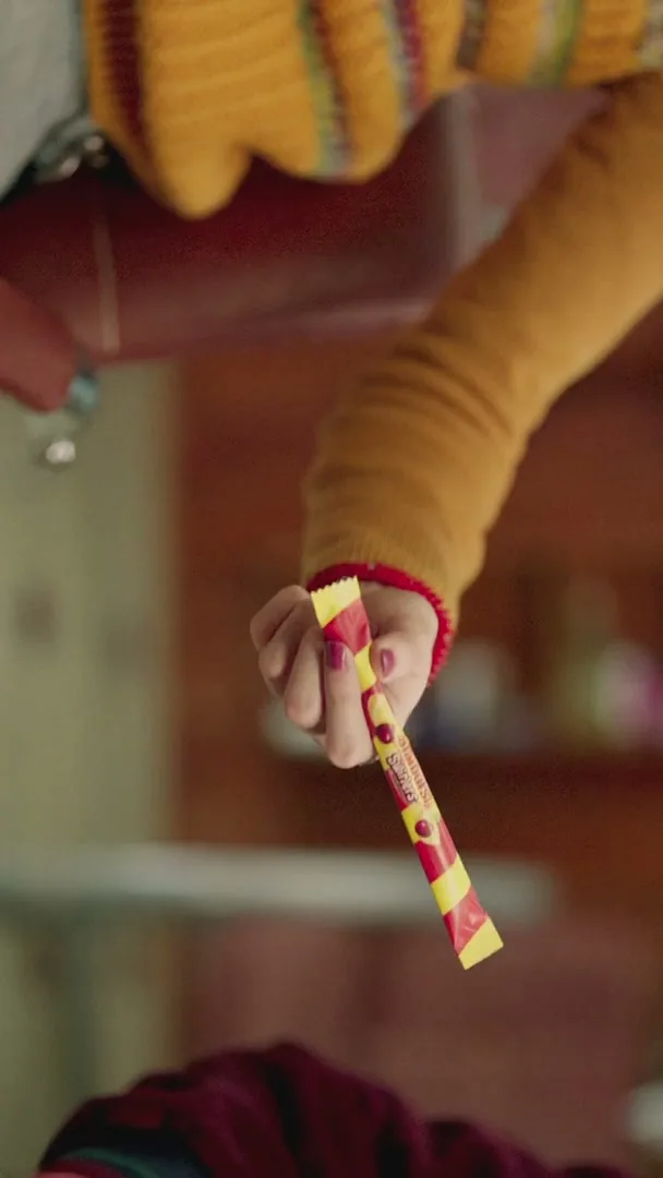 A person's arm in a yellow sweater holds a Starburst Swirlers candy, with a blurred background of a room.