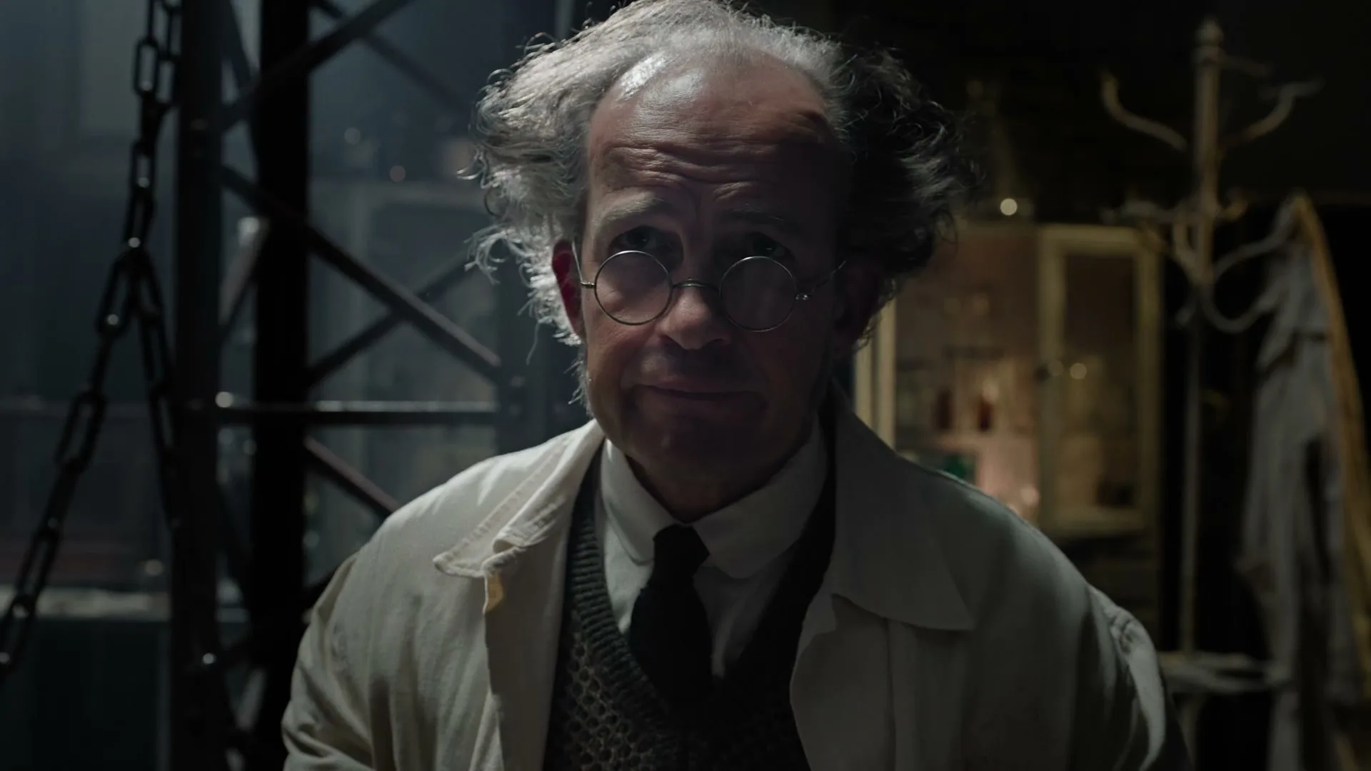 A disheveled male scientist in a lab coat holds up a children's alphabet book in a dimly lit, cluttered laboratory.