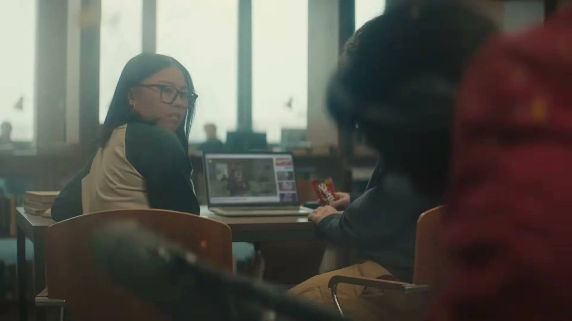 A young woman and man sit at a table in a library, looking surprised as something flies past them.