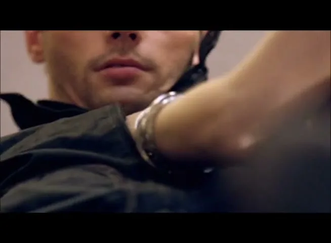 A woman's arm reaches across a man's chest, zipping up his black jacket, in a close-up shot.