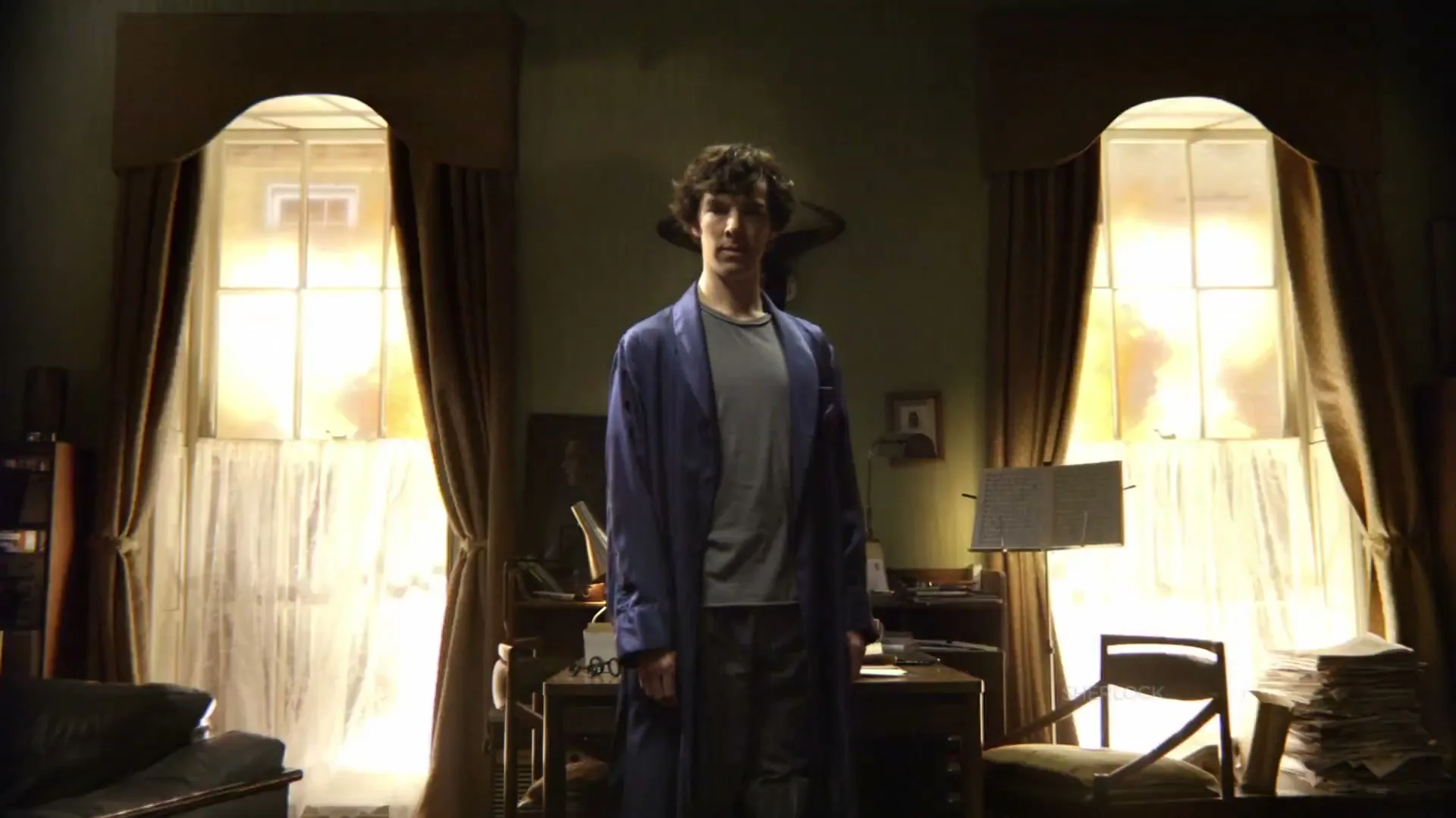 A man in a blue robe stands in a dimly lit room, then a bright light and smoke engulf him as he falls to the ground.
