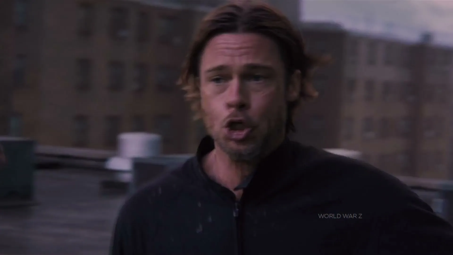 A man with a beard and curly hair runs frantically, screaming, followed by another person, on a rooftop during the day.