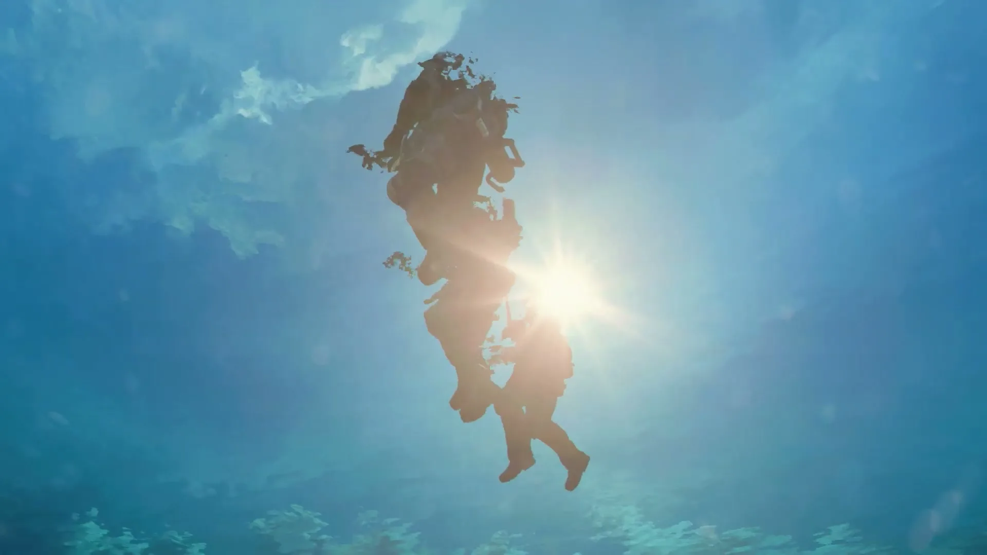 Two divers in full gear are seen from below, silhouetted against the bright sun and blue water, as they ascend through the ocean.