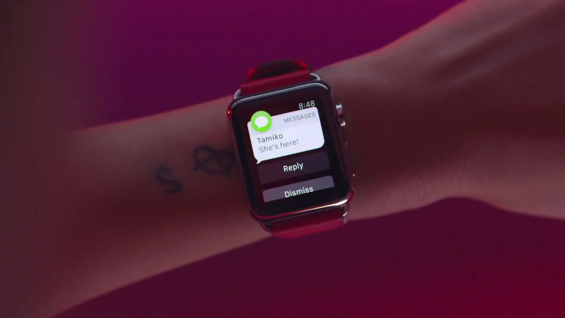 A person's arm with a red Apple Watch on their wrist, displaying a message notification on its screen.
