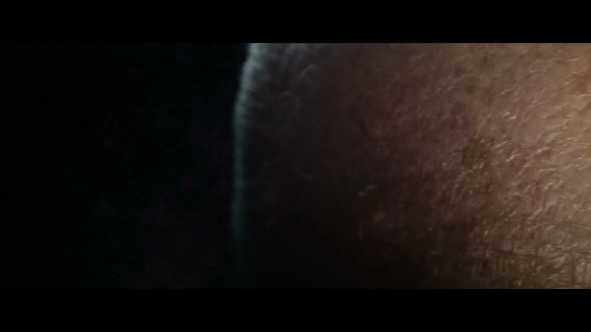 A very extreme closeup of a person's skin, possibly a face, with visible pores and hair, in a dark setting.