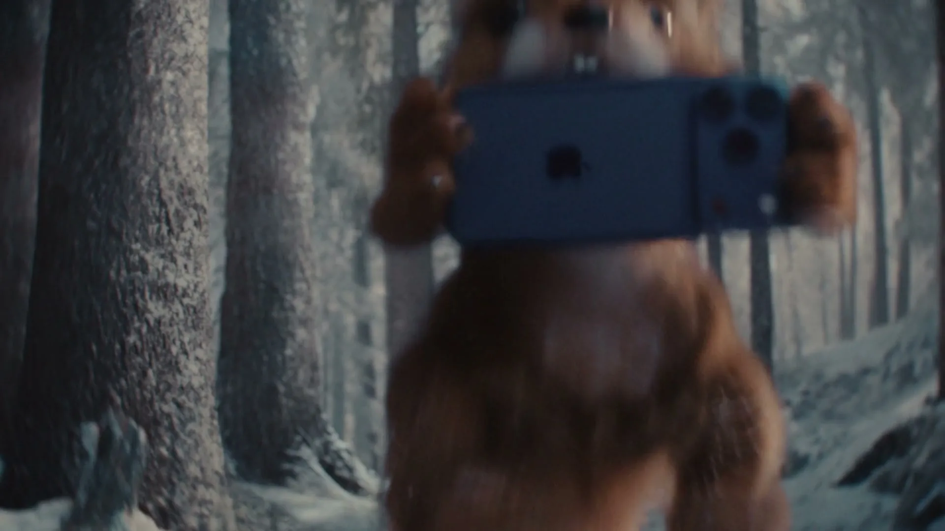A cute, furry squirrel-like creature with large front teeth holds an iPhone 15 Pro Max in a snowy forest.