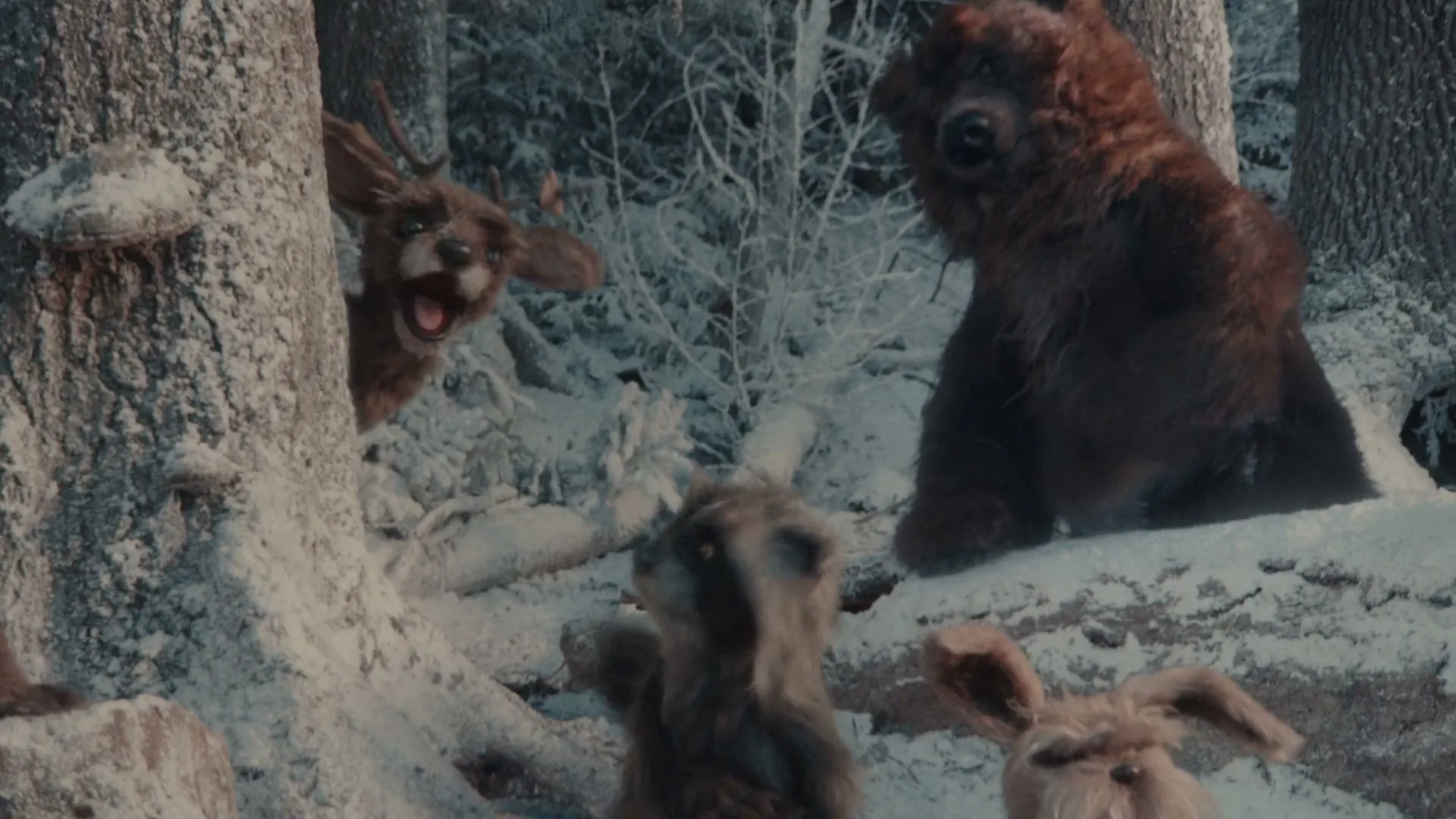 A wolf puppet with blue eyes and sharp teeth talks to a group of other animal puppets in a snowy forest.