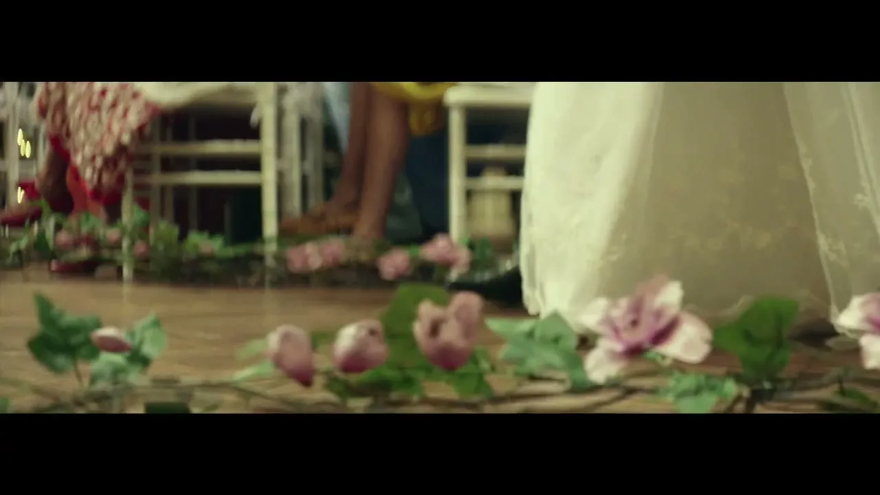A low-angle shot captures the feet of a bride and groom walking down an aisle adorned with floral garlands, as guests sit in the background.