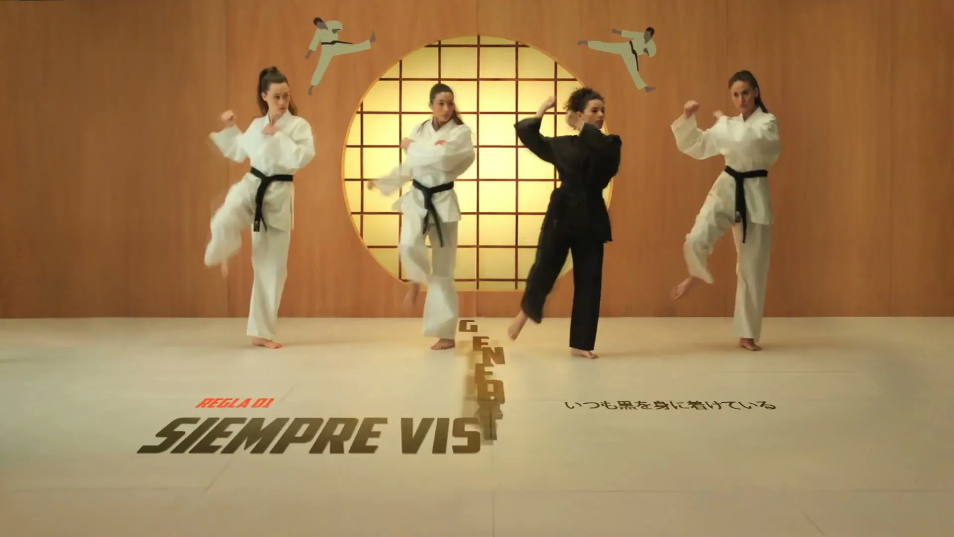 Four young women in karate gis, three white and one black, perform synchronized kicks and punches in a dojo with a circular window and stylized karate figures on the wall.
