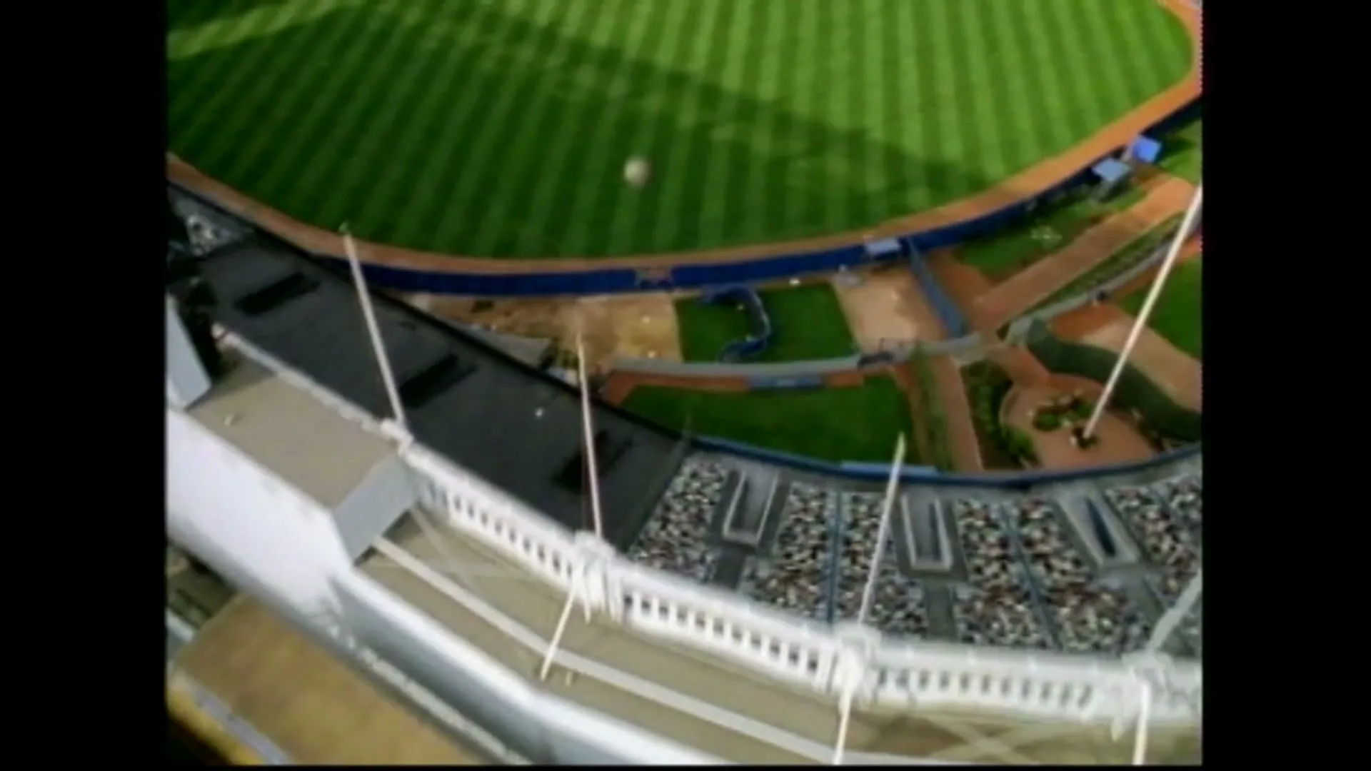 A baseball flies over the outfield of a stadium, as seen from a high angle, with the stands and field visible.