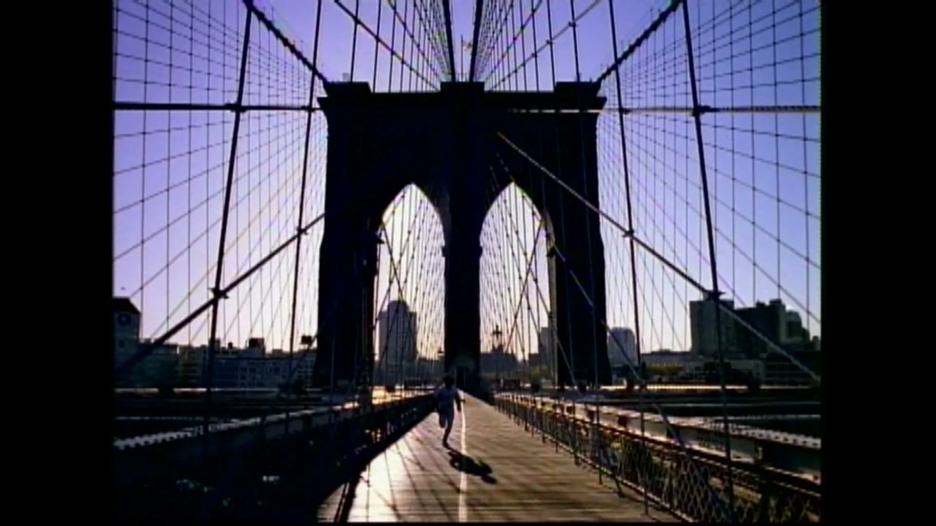 A lone runner, silhouetted against the sunrise, runs across the Brooklyn Bridge in New York City.