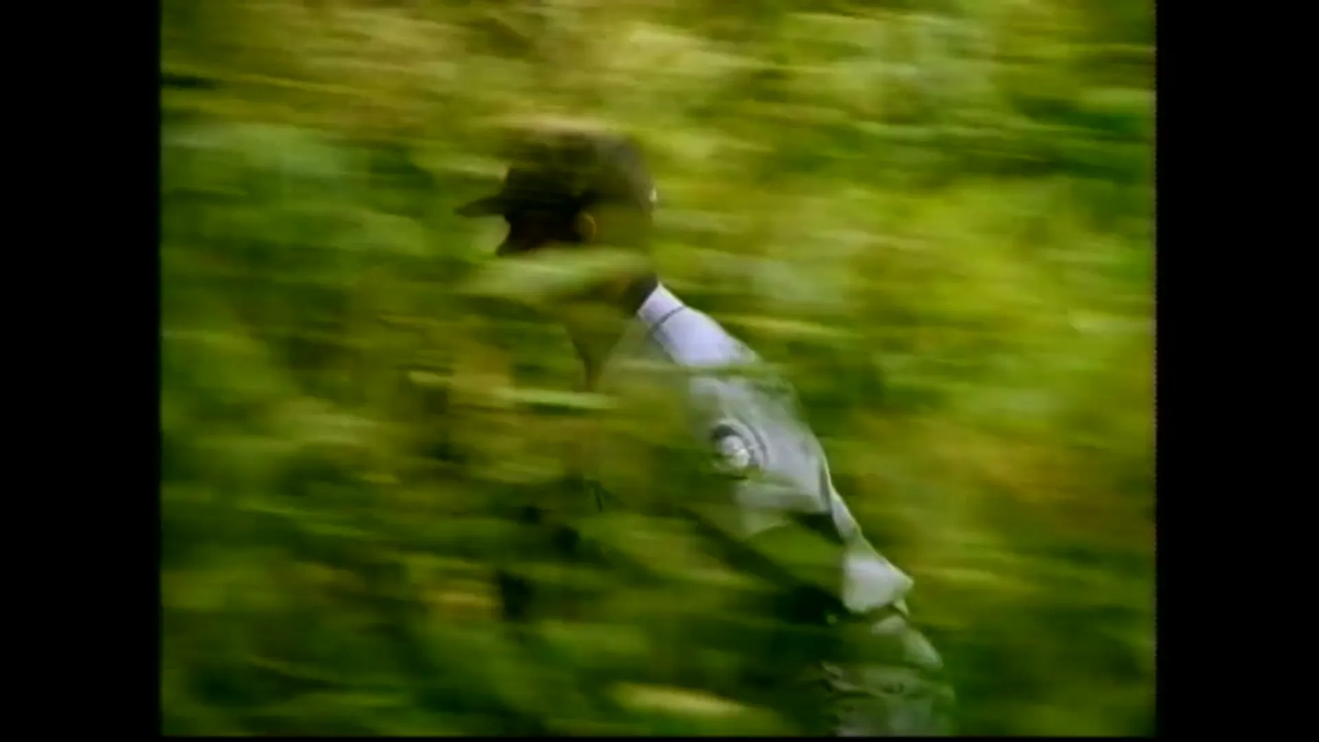 A male baseball player in a green and white uniform runs through a field of green foliage, with motion blur indicating speed.