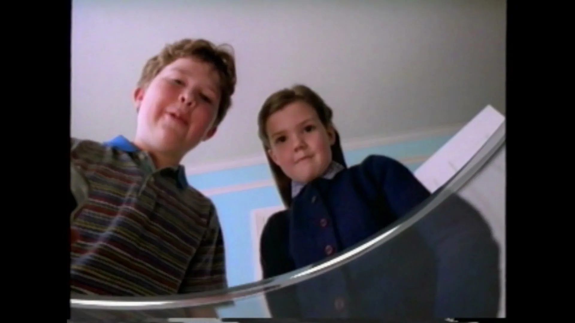 A boy and a girl look down into a fishbowl, as the boy holds a Pepsi can and drops a goldfish into the water.