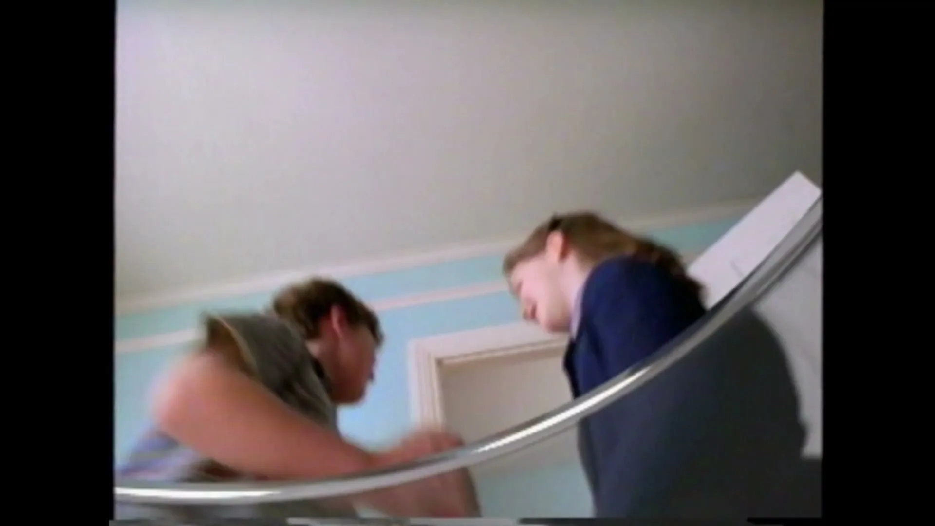 A young boy holds a Pepsi can and looks at a young girl, who is smiling, as they stand on a staircase in a house.