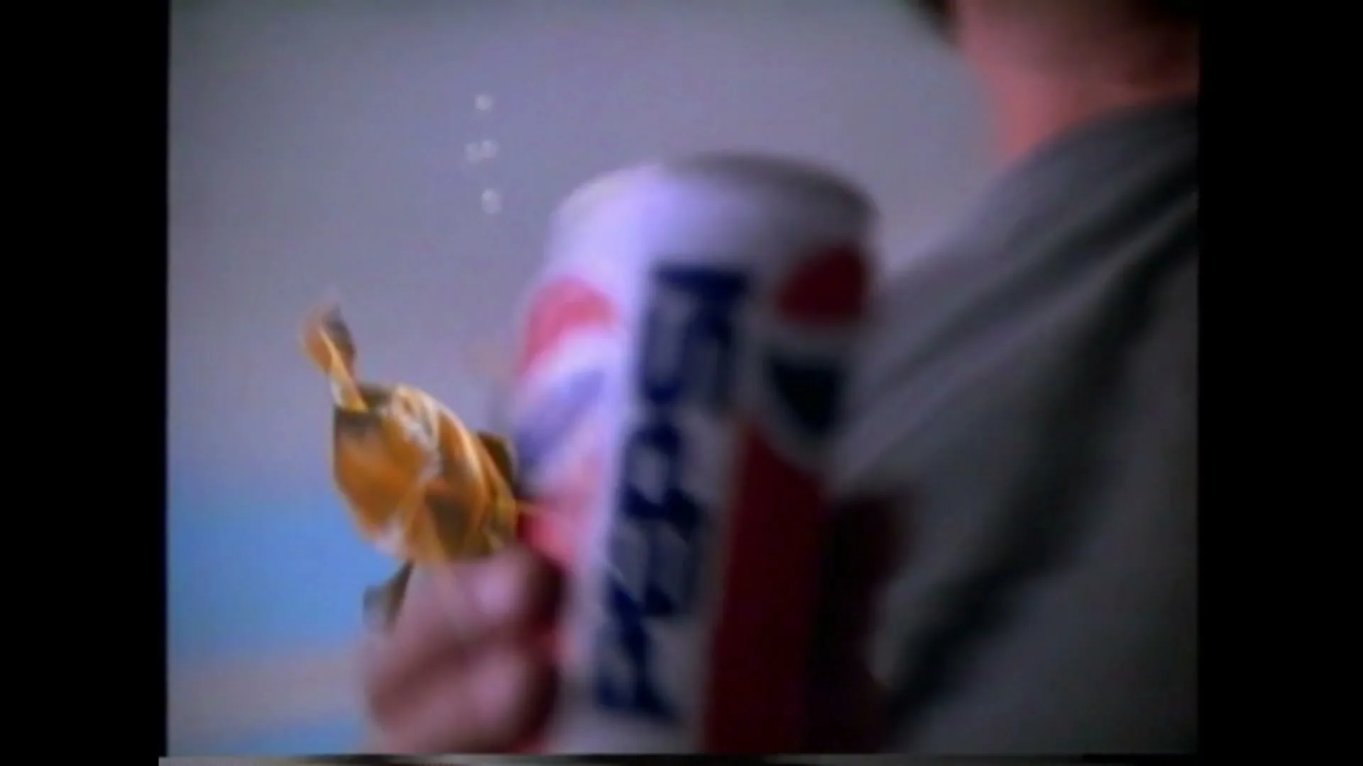 A goldfish swims towards a Pepsi can held by a person, then jumps into the can, in a bright, indeterminate interior setting.