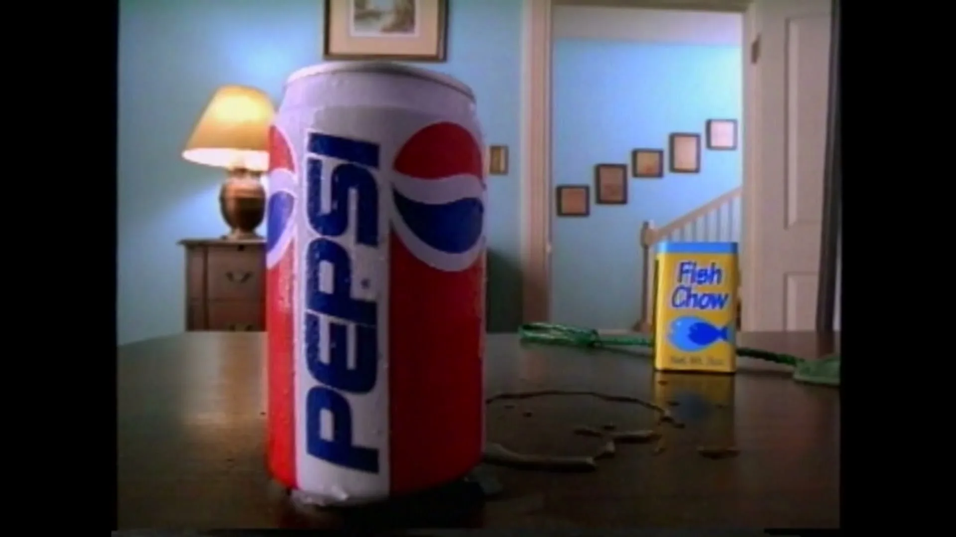 A Pepsi can sits on a table with a box of fish food and a small ball, as a child's voice asks about a fish.