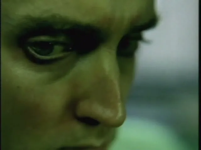 A man's face is shown in a tight closeup, with a green tint, as he looks down intently.