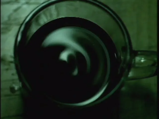 A dark liquid swirls in a clear glass mug, seen from directly above, with a green tint over the scene.