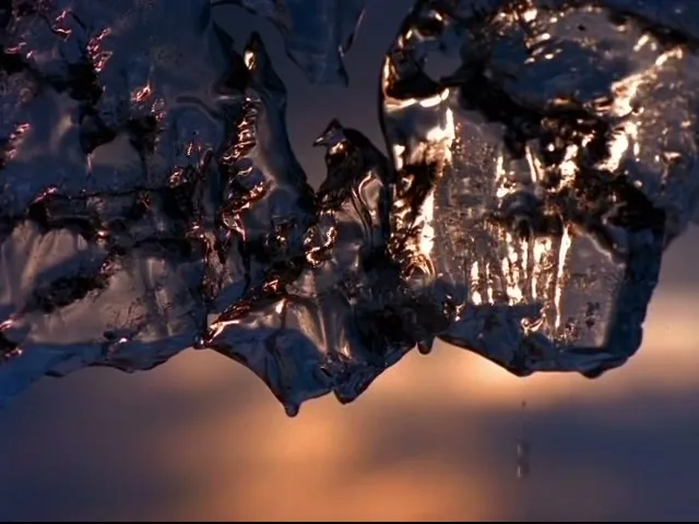A close-up shot of melting ice with a warm, blurry background, as water drips from the ice, creating a serene and natural scene.