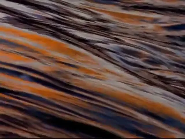 A close-up of water flowing over rocks transitions to a wide shot of a powerful waterfall cascading over snowy rocks under a dramatic sky at dusk.