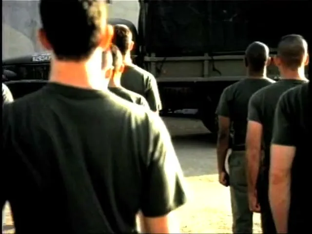 A drill sergeant in a uniform and hat holds a 6-pack of Coors Light, yelling at a line of recruits in green shirts, in an outdoor military setting.