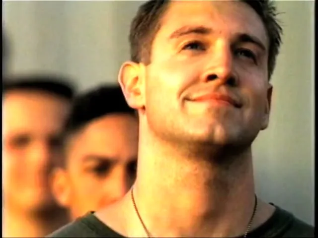 A young man in a military uniform smiles as he looks up, with other soldiers blurred behind him, before the scene transitions to a forest with mountains.