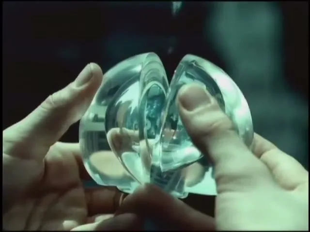 A person's hands hold a futuristic, clear, split orb, with a ghostly overlay of a person in a city background.