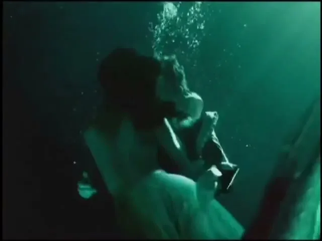 A person in dark clothing and another in light clothing are seen underwater, with bubbles rising, in a dark, mysterious setting.
