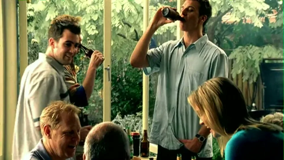 A group of friends and family gather at a casual outdoor party, drinking beer and laughing together on a sunny day.