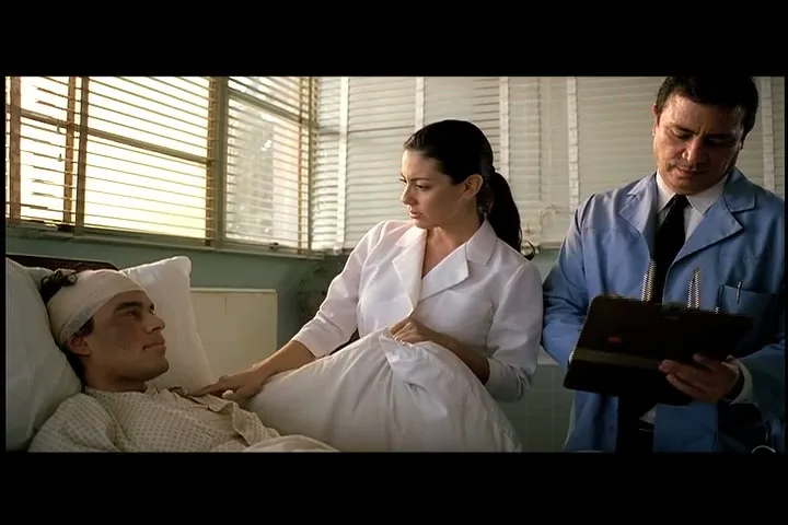 A male patient with a head bandage lies in a hospital bed, while a female nurse and a male doctor stand beside him in a hospital room.