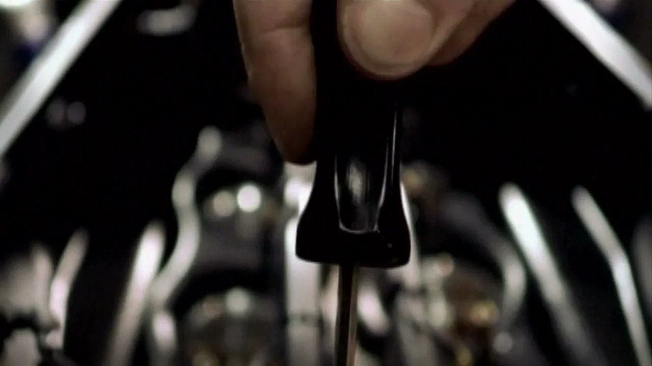 A person's hand holds a black dipstick, checking the oil level in a car engine, in a dark garage.