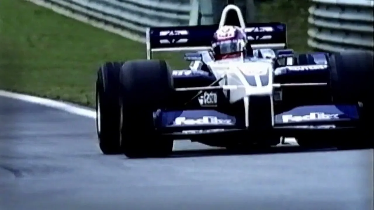 A Formula 1 race car, dark blue and white, speeds around a turn on a race track during a daytime race.