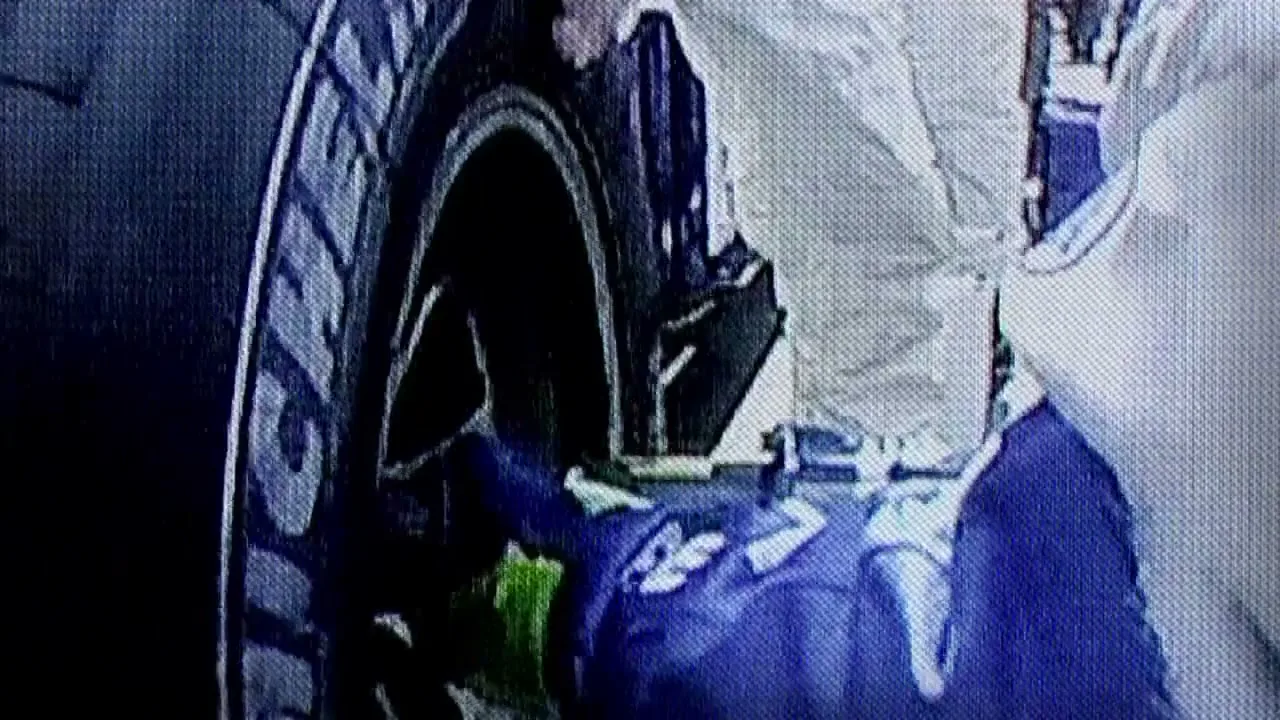 A pit crew member in a blue uniform works on the tire of a race car during a pit stop.