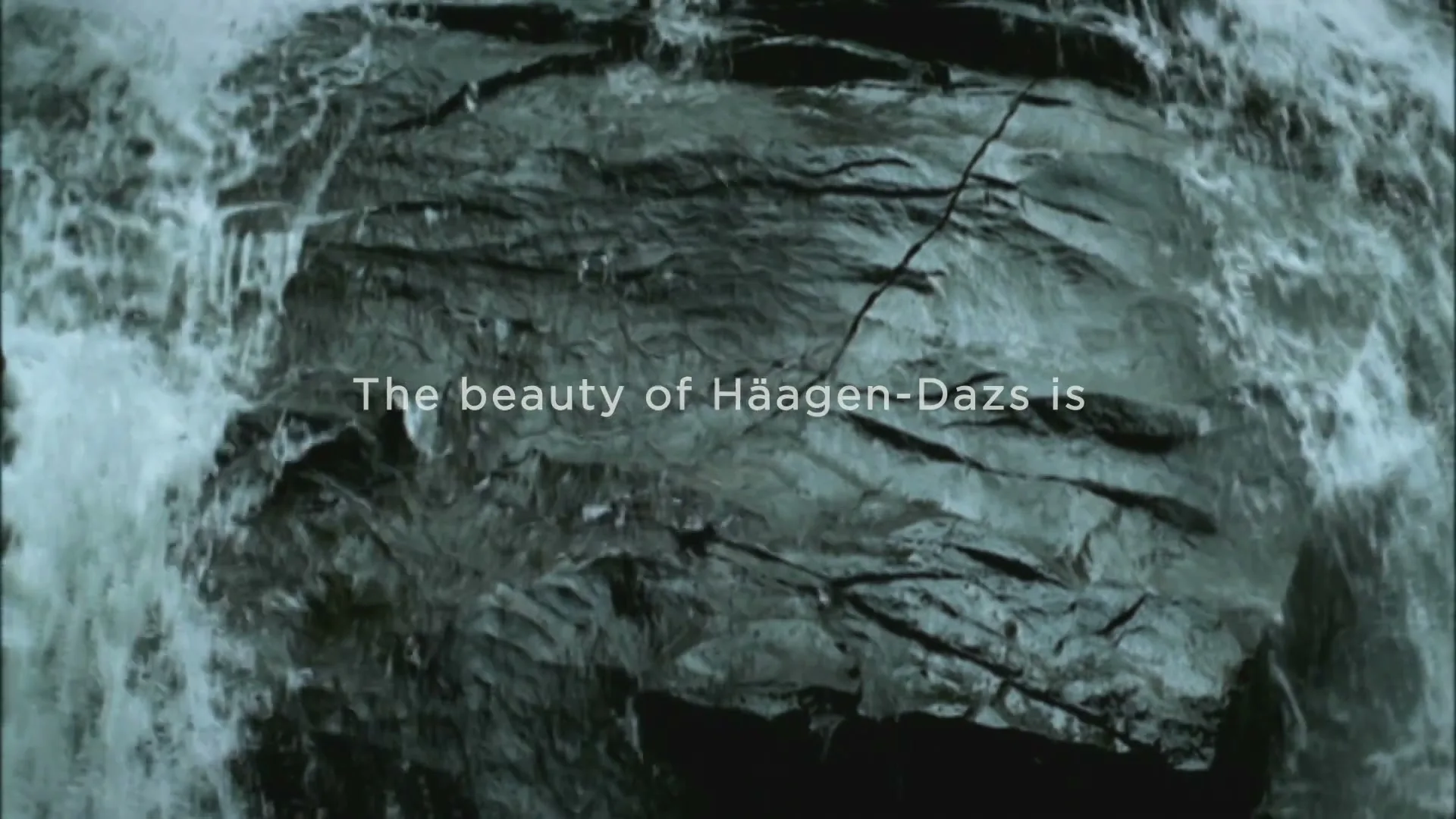 Water cascades over dark, textured rocks, with white on-screen text appearing over the scene.