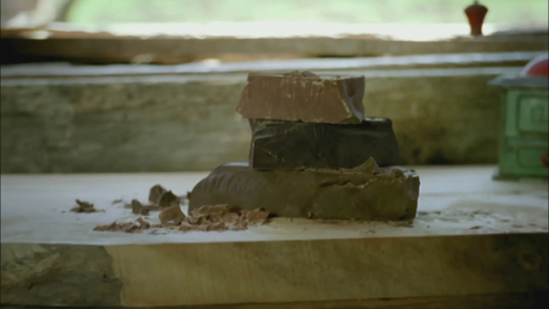 Three blocks of chocolate, varying in color, are stacked on a rustic wooden surface, with chocolate shavings scattered around them.