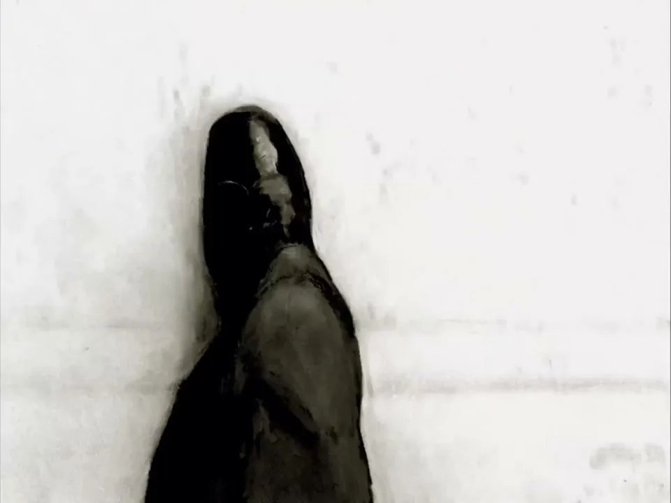 A black, shiny dress shoe is seen from above, tapping on a light-colored, textured surface in a high-contrast, black and white shot.