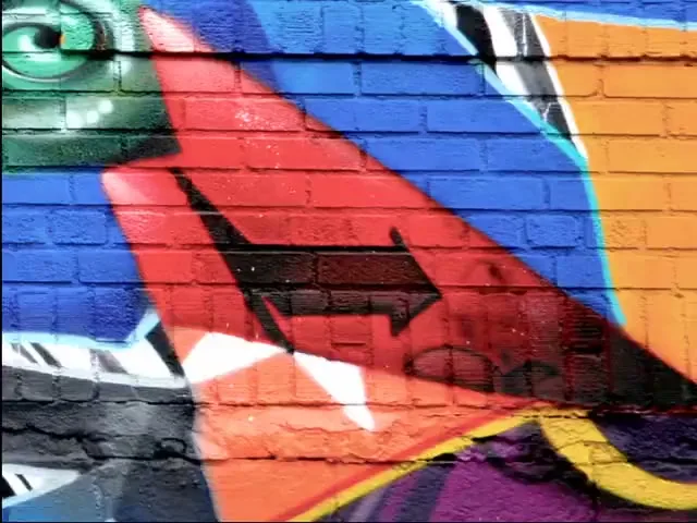 A vibrant, colorful graffiti mural with an arrow design is painted on a brick wall, showcasing urban street art.