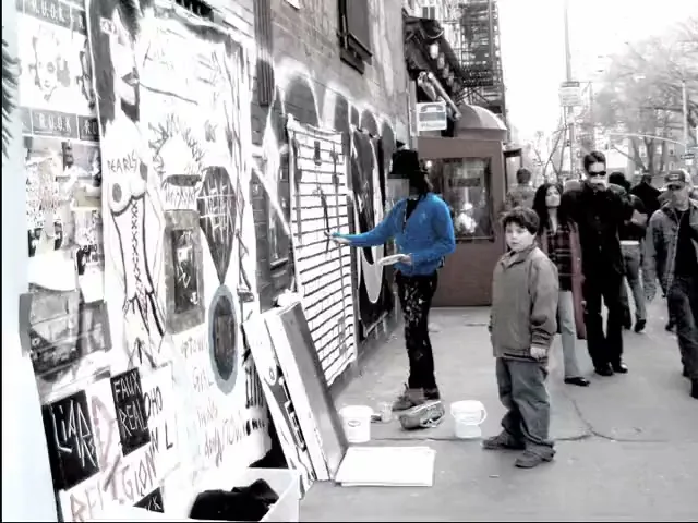 A blue electric guitar is prominently displayed among other grayscale guitars in a music store, with a sign partially visible in the foreground.