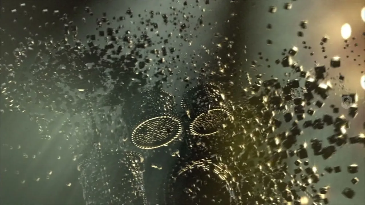 A drum kit made of small, dark, metallic cubes explodes into thousands of pieces in a dark, smoky void.