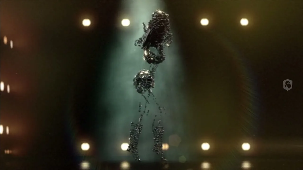 A female figure made of small, dark, metallic spheres dances on a stage with bright lights in the background.