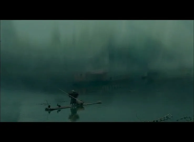 A lone fisherman in a conical hat stands on a small bamboo raft with two cormorants, fishing in a misty, serene river.