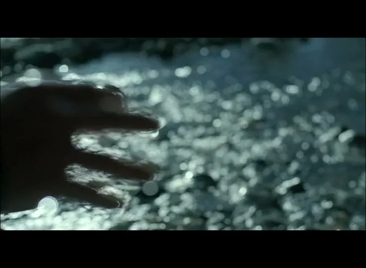 A person's hand is silhouetted as it moves through sparkling water, creating ripples and reflections.