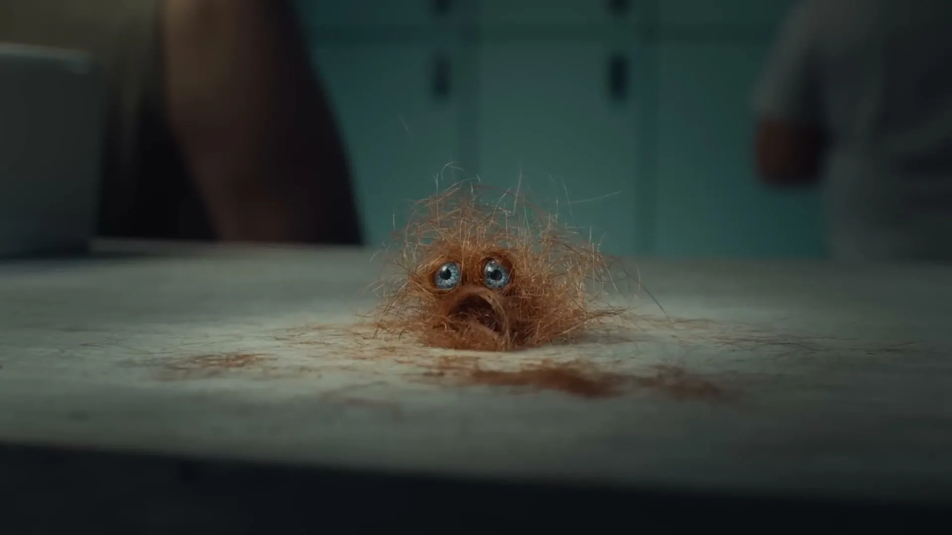 A small, sad, hairy creature with blue eyes sits on a bathroom counter, as if it has been shaved off a person.