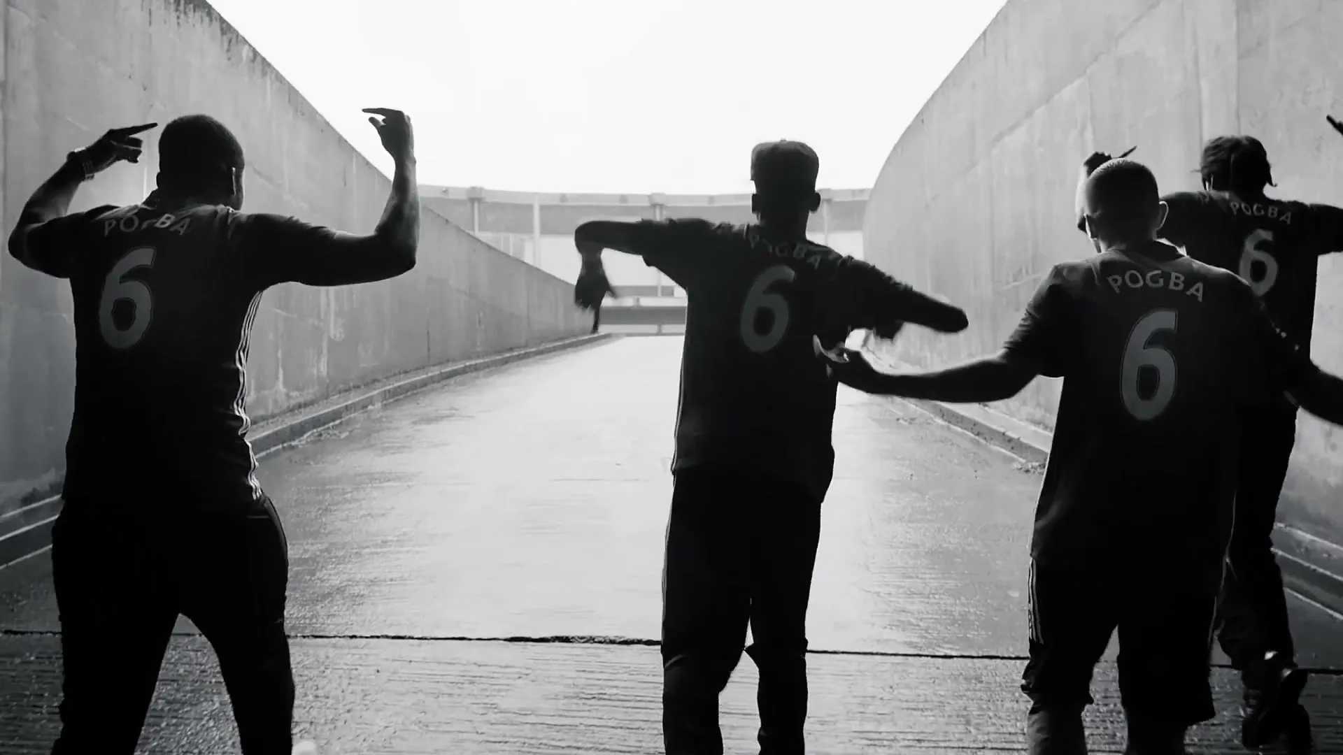 Three male soccer players, seen from behind, wearing jerseys with 'POGBA 6' on them, dance in a stadium tunnel, silhouetted against a bright exit.