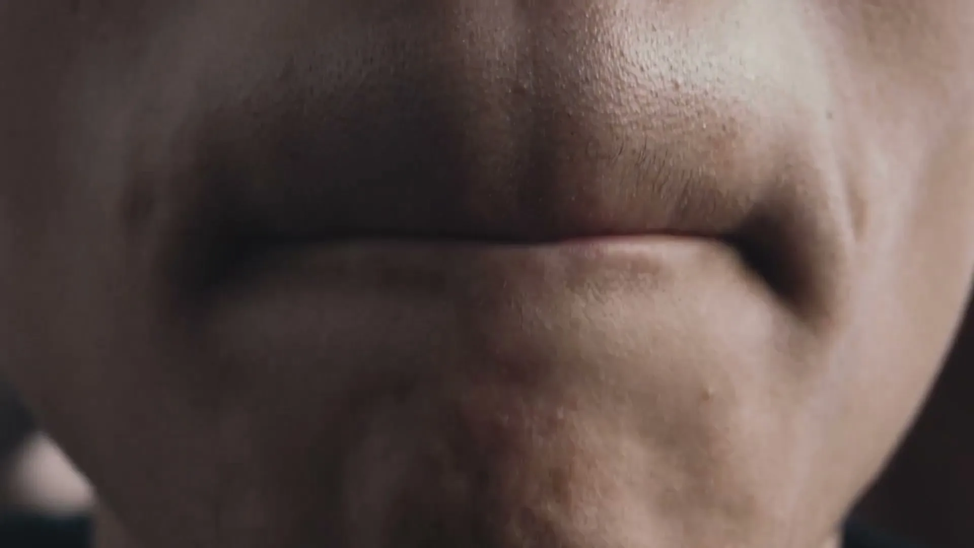 A young male's mouth is shown in extreme closeup, then the camera pulls back to reveal him among a group of excited young people.