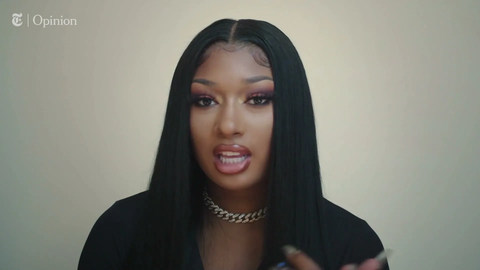 Megan Thee Stallion, a Black woman with long dark hair and a gold chain, speaks directly to the camera in a medium shot against a plain background.