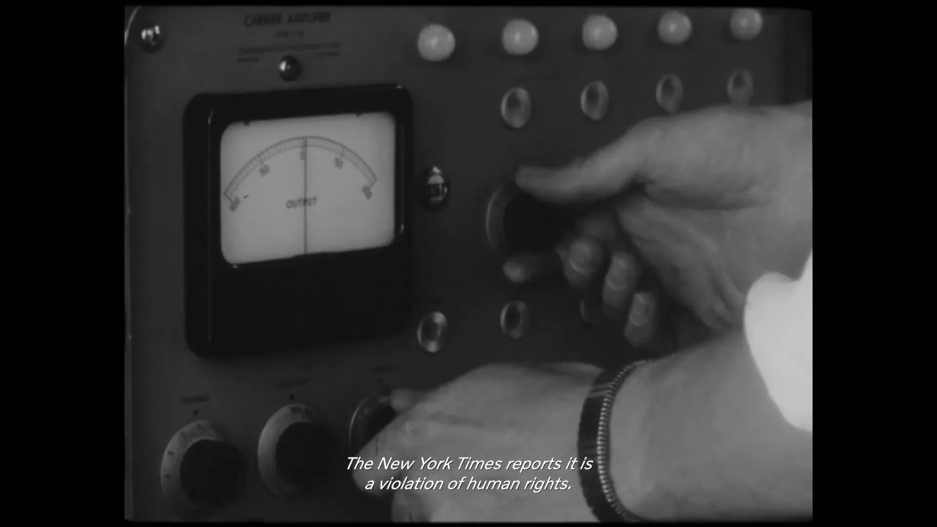 A person's hands adjust knobs on an old, analog machine with a dial, in a black and white archival shot.