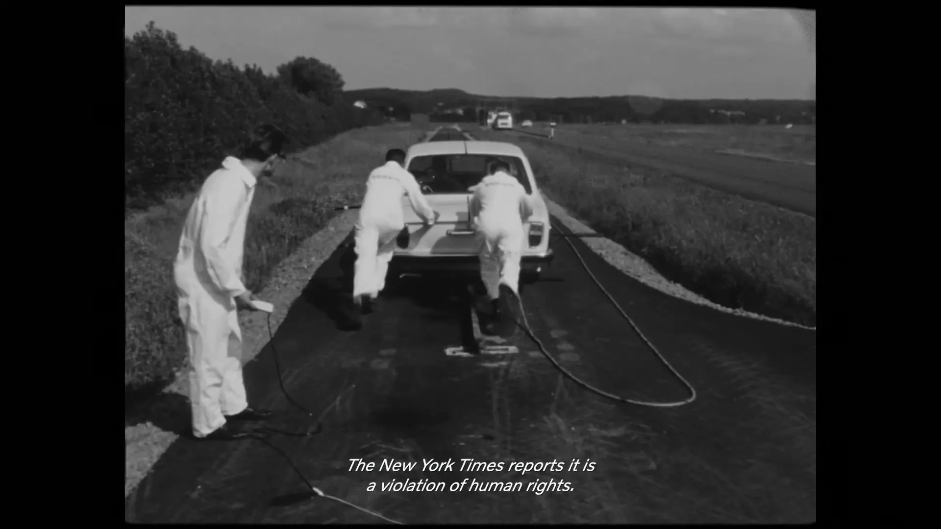 Three male engineers in white jumpsuits push a white Volvo car on a test track, then the car is shown in a crash test facility, in black and white archival footage.